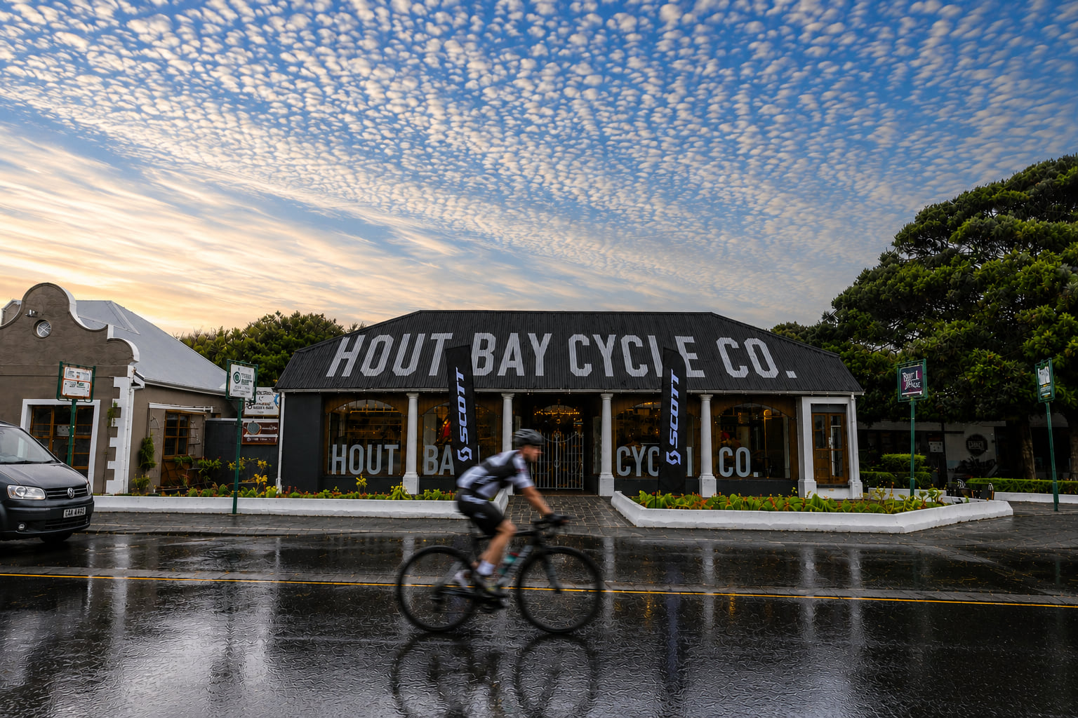 Hout Bay Cycle Co bike shop on Main Road, Hout Bay, Cape Town, with a cyclist riding past at sunrise