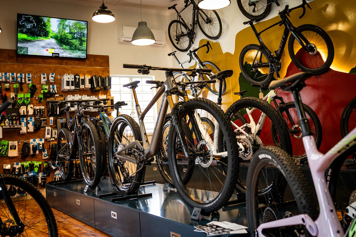 Mountain bikes lined up on the display plinth at Hout Bay Cycle Co, with the accessories wall behind